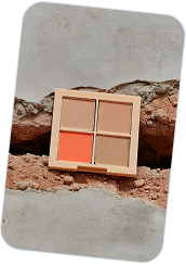 Compact eyeshadow palette with four shades including beige, brown, and orange placed on a textured stone surface.